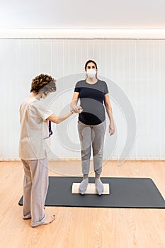 pregnant woman standing on a proprioceptive trunk for lumboabdominal and perineal walls with physiotherapist photo