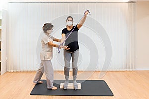 A pregnant woman standing on a proprioceptive trunk or wooden roller with an elastic band with physiotherapist