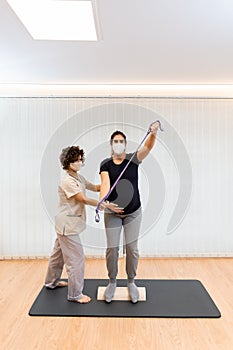 A pregnant woman standing on a proprioceptive trunk or wooden roller with an elastic band with physiotherapist