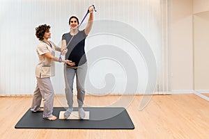 A pregnant woman standing on a proprioceptive trunk or wooden roller with an elastic band with physiotherapist