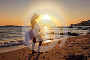 Pregnant woman stands on the beach and holds her belly during sunset time