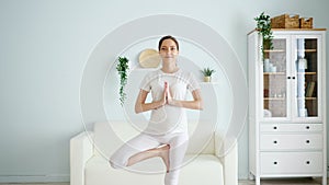Pregnant woman stands in vrksasana in spacious room at home