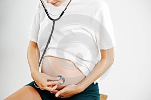 Pregnant woman with stethoscope on belly listening carefully to the baby..