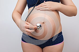 Pregnant woman with a stethoscope listens to her baby`s heartbeat