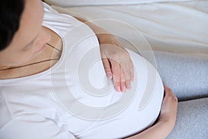 Pregnant woman stroking big belly, relaxing on bed indoors, enjoying expectation, pregnancy, dreaming on being mother