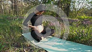 Pregnant woman stroking her baby belly sitting on grass