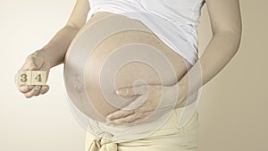 Pregnant woman stroking her belly with the pregnancy week number 34