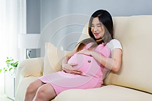 Pregnant woman stroking her belly on sofa in living room