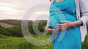 Pregnant woman stroking her belly, walks in nature