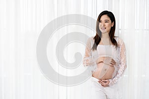 Pregnant woman stroking her belly on window background
