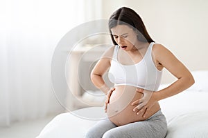 Pregnant woman suffering from abdominal pain at home, copy space