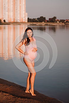 pregnant woman in a swimsuit, full-length portrait of an Asian pregnant brunette woman posing in a pink swimsuit holding