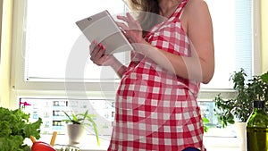 Pregnant woman with tablet pc computer preparing vegetable salad at home