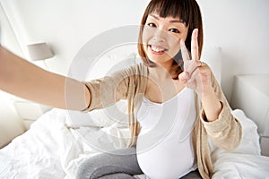 Pregnant woman taking selfie in bed at home