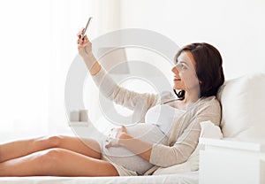 Pregnant woman taking smartphone selfie at home