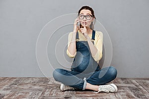 Pregnant woman talking by mobile phone and make silence gesture.