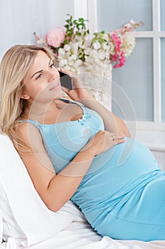 Pregnant woman talking on phone lying on bed