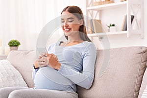 Pregnant Woman Texting On Cellphone Sitting On Sofa At Home