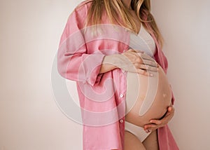 a pregnant woman third trimester in underwear and a pink shirt stands on a white background