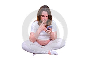 Pregnant woman thoughtfully looks at the phone in the home, isolated