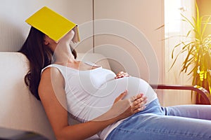 Pregnant woman tired of reading, sleeping on sofa with a book on