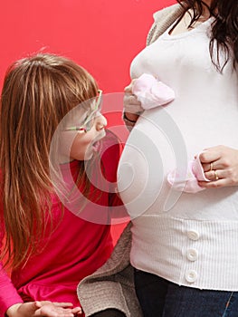 Pregnant woman with toddler girl holding baby shoes