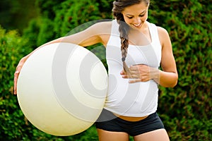 Pregnant Woman Touching Belly While Holding Fitness Ball In Park