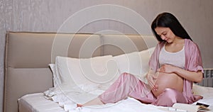 pregnant woman touching belly and sitting on the bed