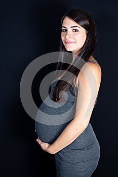 Pregnant woman touching belly under black background