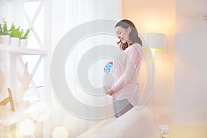 Pregnant woman touching her belly and playing with little baby shoes. Happy pregnant middle aged mother at home
