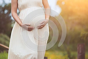 Pregnant woman touching her big belly and walking in the park