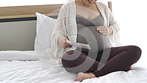 Pregnant woman touching her tummy by hand gently while looking mammogram X-ray photo on bed at home in bedroom. People lifestyles