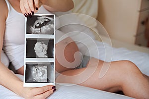 Pregnant woman with ultrasound picture of baby closeup. Snapshot of ultrasound and stomach. Pregnant on a pillow for pregnant wome photo