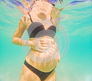 Pregnant woman underwater swimming in tropical sea. Healthy and active pregnancy. Young expecting mom on summer beach