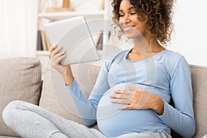 Pregnant woman using digital tablet, resting on sofa at home