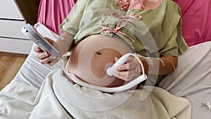Pregnant woman using fetal Doppler device for listening her baby heartbeat in hospital
