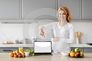 Pregnant woman using laptop in kitchen, showing nice website