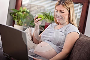 Pregnant woman using laptop and listening music