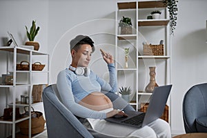 Pregnant woman using laptop relaxing at home