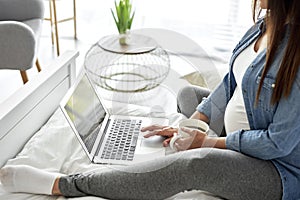 Pregnant woman using laptop while sitting on bed