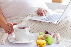Pregnant woman using laptop with tray of colorful macaroons and