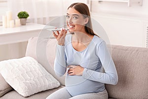 Pregnant Woman Using Smartphone Loudspeaker Sitting On Couch At Home