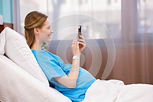 Pregnant woman using smartphone while lying in hospital bed