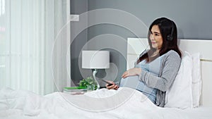 Pregnant woman using smartphone to listening music through headphones on bed