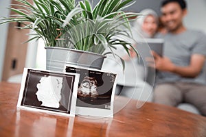 Pregnant woman using tablet pc with husband behind ultrasound on table