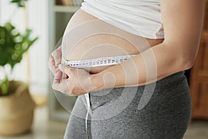 Pregnant woman using tape measure to control the abdomen