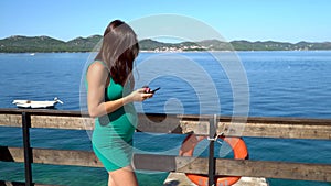 A pregnant woman waiting and checking her cellphone at sea.