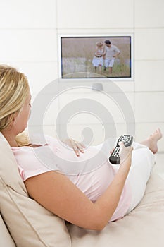 Pregnant woman watching television using remote