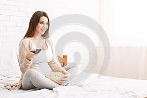 Pregnant woman watching tv at home with popcorn