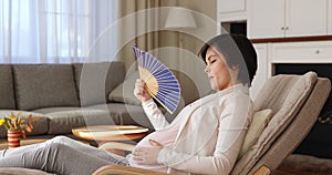 Pregnant woman waves fan suffers from heat indoor